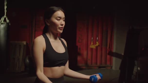 在黑暗的格斗体育馆进行运动训练时 积极进取的迷人运动适合亚洲年轻女子做哑铃式二头肌卷曲运动 锻炼上臂力量和肌肉尺寸 — 图库视频影像
