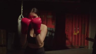 Aktif motivasyonlu spor boks eldivenli güzel bir Asyalı kadın gölge boksu eğitimi alıyor, teknikleri ve becerileri geliştiriyor, garaj jimnastik salonunda yumruk ve kroşe atıyor.