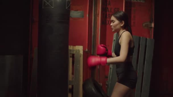 在黑暗的车库体育馆里 戴着拳击手套 靠在沙袋上 精疲力竭 不断提高拳击技术和技巧的可爱的亚洲女子已经厌倦了 — 图库视频影像