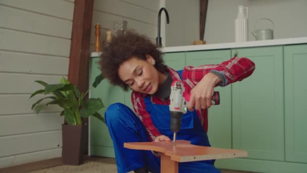 忙碌迷人的黑人女性 穿着防护服 修理旧家具 在家里做Diy工作时 用无绳螺丝刀拧开螺丝 — 图库视频影像