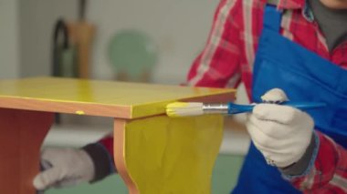 Koruyucu iş kıyafetleri içinde siyah DIY kadın yakın plan yeniden kullanım için eski mobilya yenileme ve yenileme, kapalı alanda sarı renk fırça ile boya tabure.