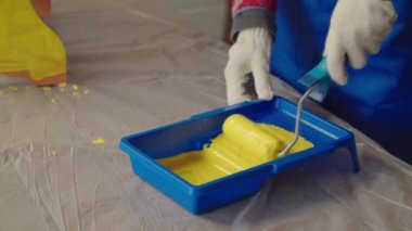 Koruyucu iş kıyafetleri giyen, mobilyaları geliştiren, evin içinde sarı renkli boya rulosu olan eski tabureyi restore eden ve boyayan bir kadın..