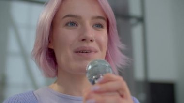 Karizmatik yetenekli, stil sahibi, çekici, pembe saçlı, mikrofonlu, neşeli şarkılar söyleyen kadın şarkıcının portresi, kapalı alanlarda pozitif titreşimler ve neşe ifade ediyor. Yakın plan..