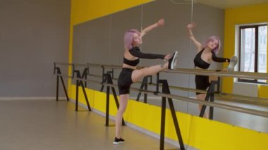 Zarif, zarif, pembe saçlı bayan dansçı dans stüdyosunda prova yaparken ısınma egzersizi yapıyor, esniyor ve bacak kaslarını esnetiyor. .