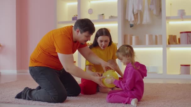快乐关心可爱的学龄前女儿 积极漂亮的父母带着婴儿 把可爱的绒毛家鼠放进运动球里 和宠物玩耍 同时让家人在室内放松一下 — 图库视频影像