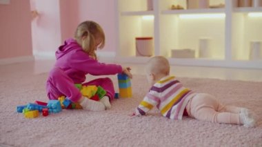 Neşeli, sevimli anaokulu kızı ve neşeli bebek eğlencenin tadını çıkarıyor, oyun geliştiriyor ve ev ortamında çocuklar inşa ederken eğleniyor..