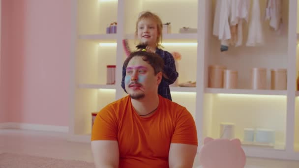 快乐积极可爱的学龄前女儿在家里玩美容院游戏的时候 用有趣的美容美发和大梳子给快乐俊俏的爸爸梳头 — 图库视频影像