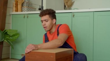 Koruyucu iş kıyafetleri içindeki yakışıklı Afro-Amerikan adam DIY mobilya montajı, çekiçle komodinin arka duvarına çivi çakma.