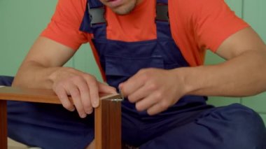 Koruyucu iş kıyafetleri içindeki yetenekli, meşgul, yakışıklı Afro-Amerikan genç işçinin portresi. Ev eşyaları kullanarak ahşap mobilyaları bir araya getirmek..