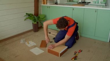 Koruyucu iş giysisi içindeki yetenekli ve yakışıklı siyahi bir adamın komodinin yan çekmecesini monte ederken, çekmece slaytları yerleştirirken ve evde tornavida kullanarak vidaları sıkarken yüksek açılı görüntüsü..
