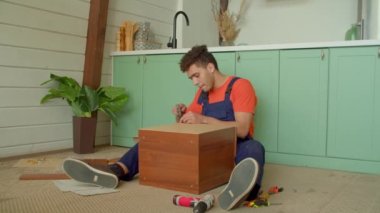 Yoğunlaştırılmış çekici Afrikalı Amerikalı tamirci komodinin yanındaki tahta paneli manuel çekiçle çiviliyor, evde yerde otururken DIY mobilyalarını birleştiriyor..