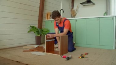 Koruyucu iş elbisesinde becerikli bir siyah tamirci DIY mobilyalarını monte ediyor, çekiçle komodinlere tahta çiviler çakıyor ve yurt içinde boş zaman geçiriyor..