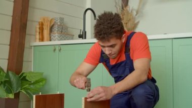Koruyucu iş giysisindeki yetenekli siyah erkek boyanın portresi DIY mobilya montajı, komodindeki ahşap pervazları çekiçle çivileme..