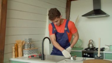 Koruyucu iş kıyafetleri ve eldivenler üreten yetenekli Afro-Amerikan erkek tesisatçı, eski bozuk lavabo süzgecini değiştirip yerli mutfakta tornavida kullanarak monte ediyor..