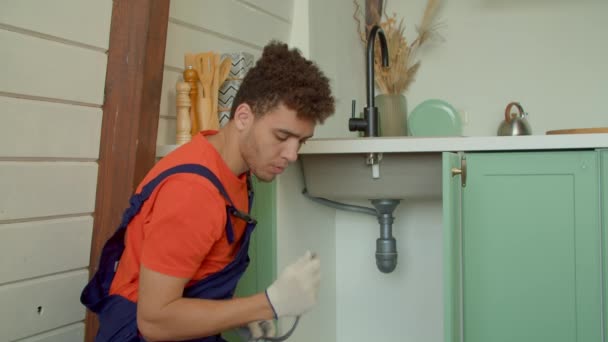 保護作業着固定キッチン蛇口でプロの魅力的なアフリカ系アメリカ人配管サービスを屋内で提供しながら 柔軟な水道管を交換してインストール — ストック動画