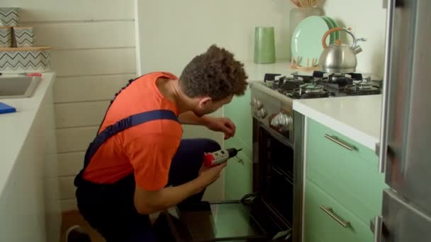 专业英俊的黑色修理工 穿着工作服 为顾客提供服务支持 在家用厨房用无绳电钻螺丝刀修理厨房烤箱 — 图库视频影像