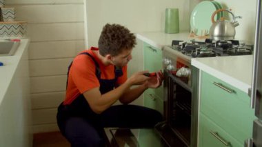 Yetenekli, konsantre ve yakışıklı Afro-Amerikan erkek teknisyen servis işi yapıyor, mutfak fırını kuruyor ve ev mutfağında tornavida kullanarak vidaları tamir ediyor..
