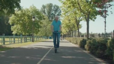 Aktif yaşam tarzı çekici olgun bir adam eğlence peşinde koşuyor, park alanında elektrikli scooter kullanıyor ve güneşli bir günde güzel yaz doğasının ve eğlencenin tadını çıkarıyor..