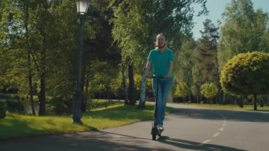 Aktif, sağlıklı bir yaşam tarzı. Bisiklet kasklı güzel bir kadın. Park yolunda e-scooter kullanıyor, güneşli bir günde yaz tatillerini dışarıda geçirirken boş zamanların ve manzaranın tadını çıkarıyor..