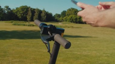 Yetişkin erkek ellerinin e-scooter kiralamak için cep telefonu uygulamasını kullanması, yaz parkında dolaşmak için QR kodu ile çevrimiçi ödeme.