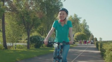 Aktif, sağlıklı bir yaşam tarzı. Kasklı, kasklı, bisikletli güzel, olgun bir kadın. Park yolunda bisiklet sürüyor, boş zamanların ve manzaranın tadını çıkarıyor..