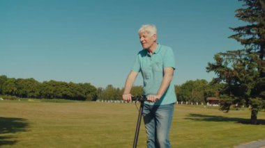 Aktif yaşam tarzının portresi günlük giysiler içinde olgun bir adam halka açık bir parkta elektrikli scooter kullanıyor, eğlence ve yaz kovalamacasının tadını çıkarıyor, mutluluk, pozitiflik ve neşe ifade ediyor.