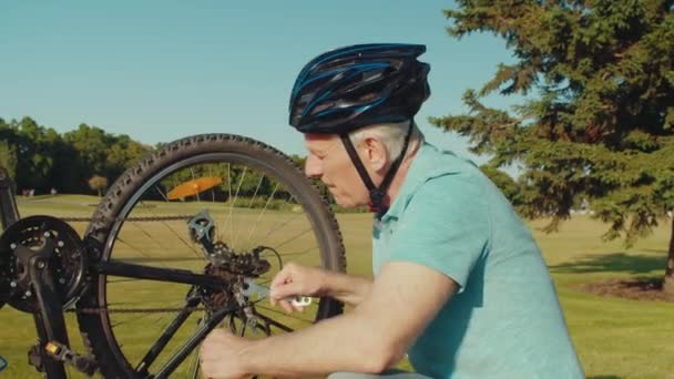 美しい夏の自然の中で自転車に乗っている間 熟練したハンサムな引退した男性の肖像画は 自転車の後輪やスパナでブレーキを固定し 修理をチェックします — ストック動画