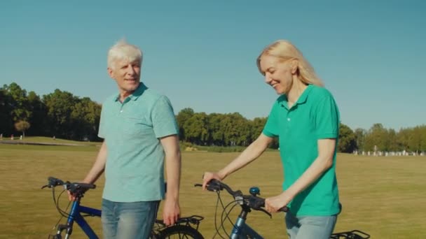一对成熟的骑自行车的快乐而放松的骑车人的画像 他们过着积极的生活方式 在公园的草坪上散步 在一起享受暑假时表现出愉快的心情和欢乐 — 图库视频影像