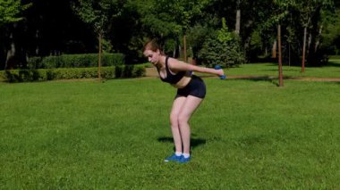 Kol kaslarını güçlendirme ve güçlendirme egzersizleri yapan, park yeşili çimlerinde ağırlık çalışması yapan, motive edici, sportif formda bir kadın..