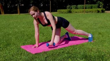 Aktif motivasyonlu güzel atletik fit orta yaşlı kadın fitness minderi üzerinde kaçak sıra egzersizi yapıyor, üst vücut gücünü arttırıyor ve dışarıda egzersiz yaparken çekirdek dengesini arttırıyor..