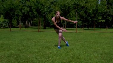 Aktif motivasyona sahip orta yaşlı spor giyimli çekici kadın park yeşili çimenliğinde egzersiz yapıyor. Açık havada vücut çalışırken kalça kaslarını, kaslarını ve iç kaslarını güçlendiriyor..