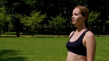 Aktif, pozitif, orta yaşlı, spor kıyafetli güzel bir kadın park yeşil çimlerinde kollarını kavuşturmuş, dostça gülümseyerek motivasyon, güven ve kararlılığı ifade ediyor..