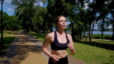 Etkileyici kararlı sportif fitness orta yaşlı bayan koşucu kardiyo antrenmanı yapıyor, güneşli yaz gününde açık havada spor yaparken yeşil parkta koşuyor..