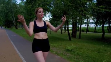 Aktif giyimli canlı yayın videosundaki çekici kadın spor yaptıktan sonra parkta yürürken cep telefonu kullanıyor, internetteki izleyicilerle iletişim kuruyor ve aktif yaşam tarzını paylaşıyor..