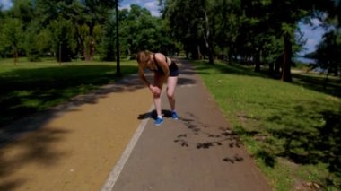 Aktif güdümlü çekici atletik formda bir bayan koşucu dizinden sakatlanıyor, dizkapağına masaj yapıyor, dışarıda koşu antrenmanı yaparken ağrıyı dindirmeye çalışıyor..
