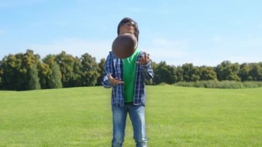 Siyah gözlü, Amerikan futbolu topu tutan yakışıklı Afro-Amerikan okul çocuğunun portresi. Arkadaşça gülümseyen, pozitifliğini ve mutluluğunu ifade eden yeşil sahada oyun oynarken..