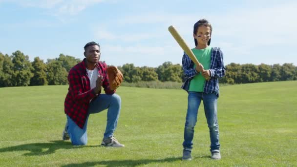 アクティブな愛らしい学校の年齢 アフリカ系アメリカ人の少年野球選手 興奮する黒人の父親のキャッチャー 野球の試合をするグローブ 自然の中で家族が余暇を過ごしながらグリーンフィールドでピッチを戦う — ストック動画