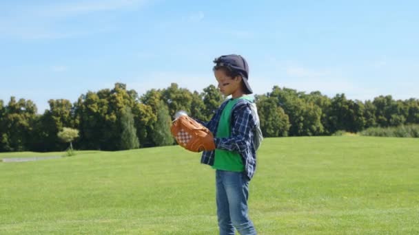 意欲的な動機づけられたかわいい学校時代の黒人の少年ピッチャー眼黒と野球の手袋を着て 緑の草場で野球の試合をしながらボールを投げる — ストック動画