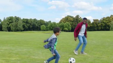 Olumlu tatlı Afro-Amerikan çocuk ve neşeli siyah baba futbol oynuyor, futbol topu paslıyor ve jestleri kazanarak golü kutluyor parkta boş zamanların tadını çıkartıyor..