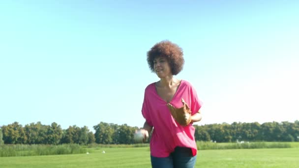 アクティブなかなりアフリカ系アメリカ人女性野球選手 緑のフィールドでカーリーヘアのゲームをプレイし パブリックパークで夏の日にアクティブなライフスタイルとレジャーを楽しんでいる間 グローブにボールをキャッチ — ストック動画