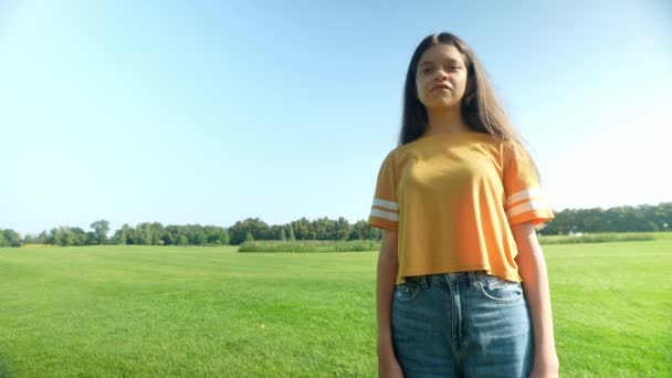 美丽而笔直的棕色长发 可爱的拉美裔少女 站在绿地上 面带微笑 在夏日公园里悠闲自在地表达着幸福和欢乐 — 图库视频影像