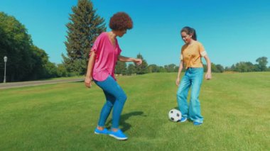 Kaygısız Afrikalı Amerikalı anne kıvırcık saçlı ve neşeli, çoklu etnik kökenli genç kız eğleniyor, futbol oynuyor, koşuyor ve yaz parkında futbol topu paslıyor..