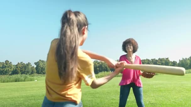ポジティブな魅力的なアフリカ系アメリカ人の母親 キュリーな髪と素敵な多人種間の十代の少女は一緒にレジャーやスポーツ活動を楽しんで 公共の公園でグリーンフィールドで野球の練習 — ストック動画