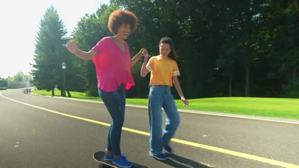 ハッピーケアフリー魅力的なアフリカ系アメリカ人の母親は 熟練した陽気な多民族の娘スケートボーダーからのサポートでスケートボードに乗ることを学び 家族は屋外でリラックスしながら — ストック動画