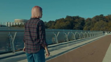 Pozitif trend görünümlü, havalı pembe saçlı, sıradan elbiseli genç kadın yaya köprüsünde paten kayıyor, aktif yaşam tarzının, özgürlüğün ve gün doğumunda şehir ortamlarında boş vakitlerin tadını çıkarıyor..