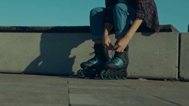 Aktif kadın patencinin düşük kesimi bankta oturur, gün doğumunda şehir caddesinde paten kaymaya hazırlanırken inline paten giyer..