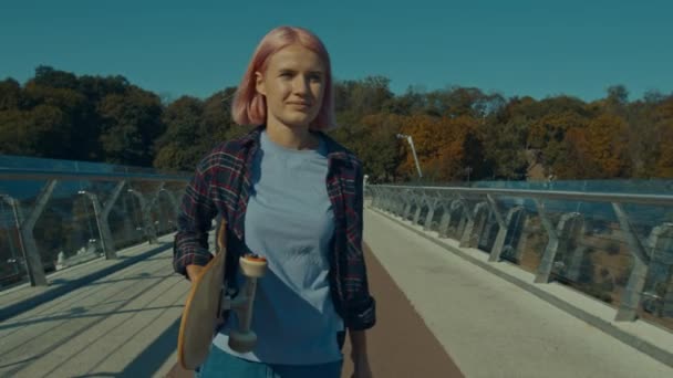 Wanita Berambut Merah Muda Yang Gembira Memegang Skateboard Berjalan Sepanjang — Stok Video
