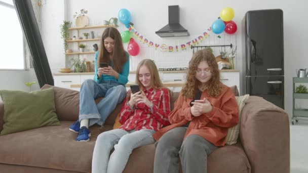 沉迷于吸引人的少女坐在沙发上 在智能手机上联网和浏览社交媒体内容 在家里庆祝生日时互相打电话 — 图库视频影像
