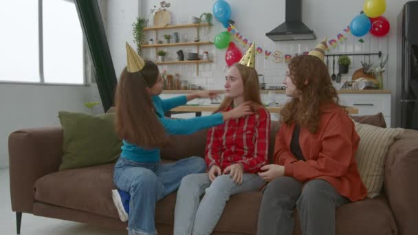 快乐而可爱的少女们坐在沙发上 享受着闲暇和带着生日帽的乐趣 在家里庆祝生日的时候表达着无忧无虑的心情和欢乐 — 图库视频影像