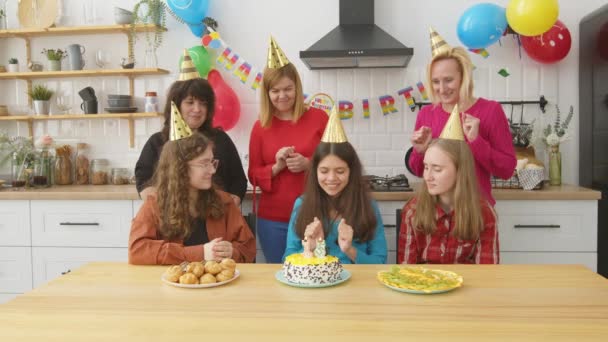 在喜庆的晚会上 戴着派对帽的可爱少女与快乐的母亲和可爱的少女朋友一起庆祝活动 并在生日蛋糕上放蜡烛 — 图库视频影像
